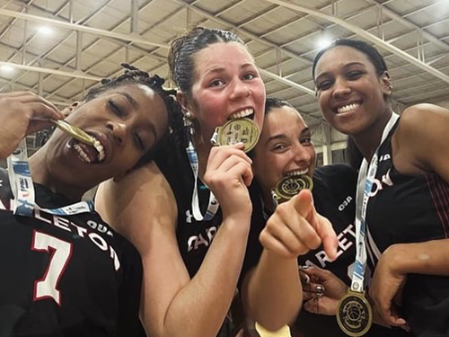 Four Women's Basketball players hold up gold medals.
