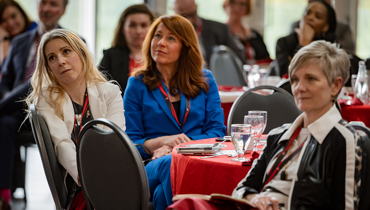 A crowd of people seated at tables listen to a speech