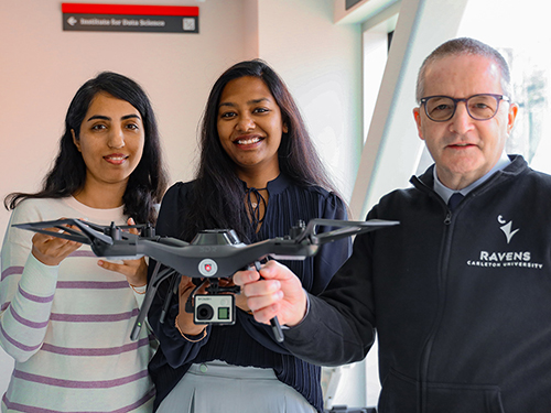 Three people pose for a photo holding a drone.