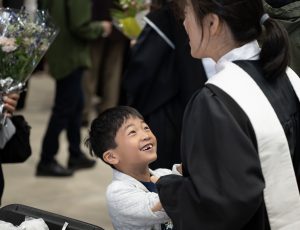 A child smiles at a woman in a graduation gown.