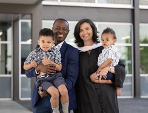 A recent graduate poses with her partner and two children outside the Athletics building.