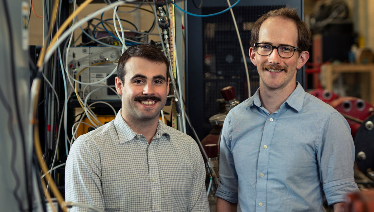 Zachary Milani and Simon Festa-Bianchet pose in their lab surrounded by electronic gear and monitoring equipment.