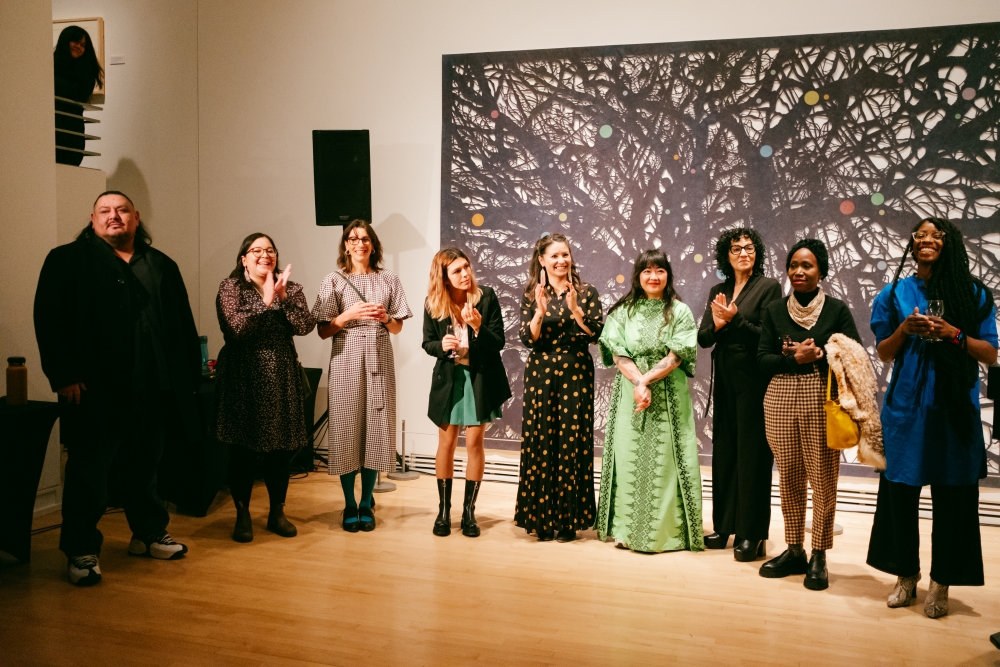 Group of people standing side by side clapping in front of art gallery exhibit.