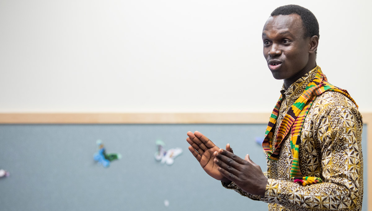 A man in a colourful shirt and a tradition scarf presents during the Climate Change Conversations.