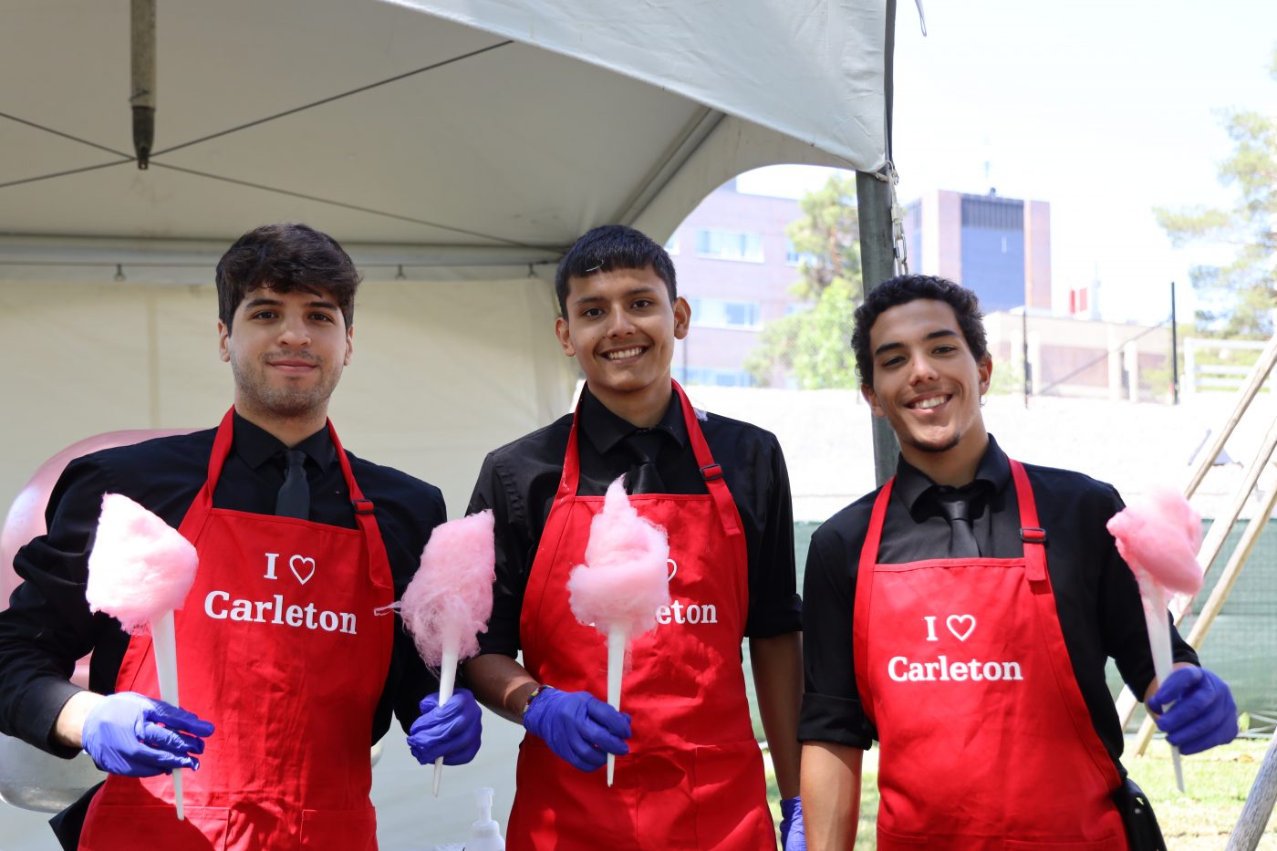 Three men wear red aprons and hold cotton candy