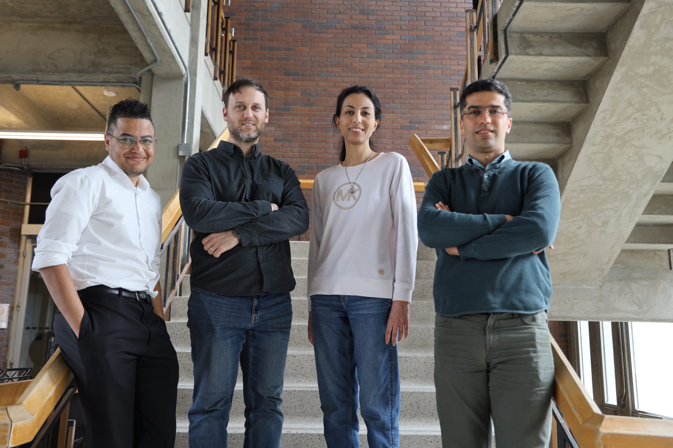 Reza Kholghy stands with three fellow researchers on a stair case. 