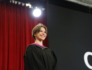 A woman with brown hair in a Convocation gown smiles at the camera