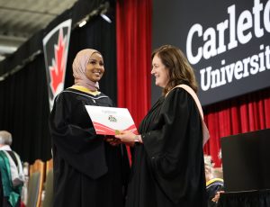 A woman smiles and shakes hands with another woman while accepting her degree
