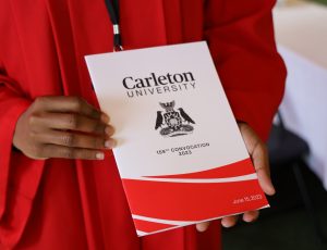 The Spring 2023 Carleton Convocation booklet is being held by someone wearing a red gown