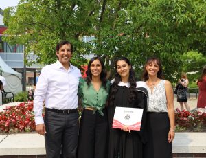 A group of Carleton graduates pose outside by a tree and smile at the camera