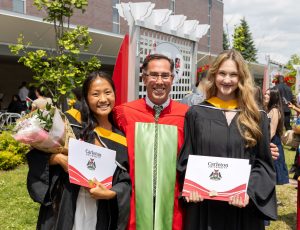 A professor and two students take a photo outside following a convocation ceremony.