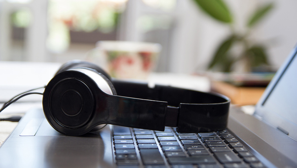 A pair of headphones lays on the keyboard of a laptop