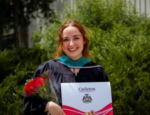 A student smiles as she poses with her degree.