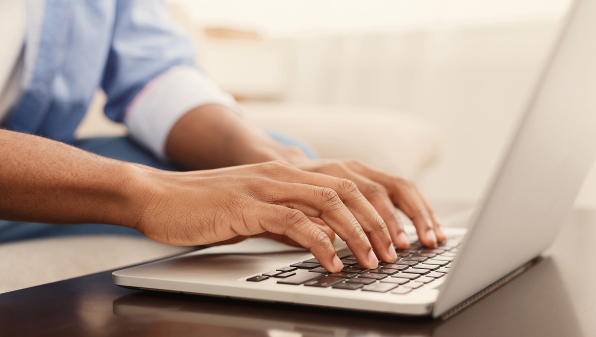 A close up image of a person's hands typing on a computer at home.