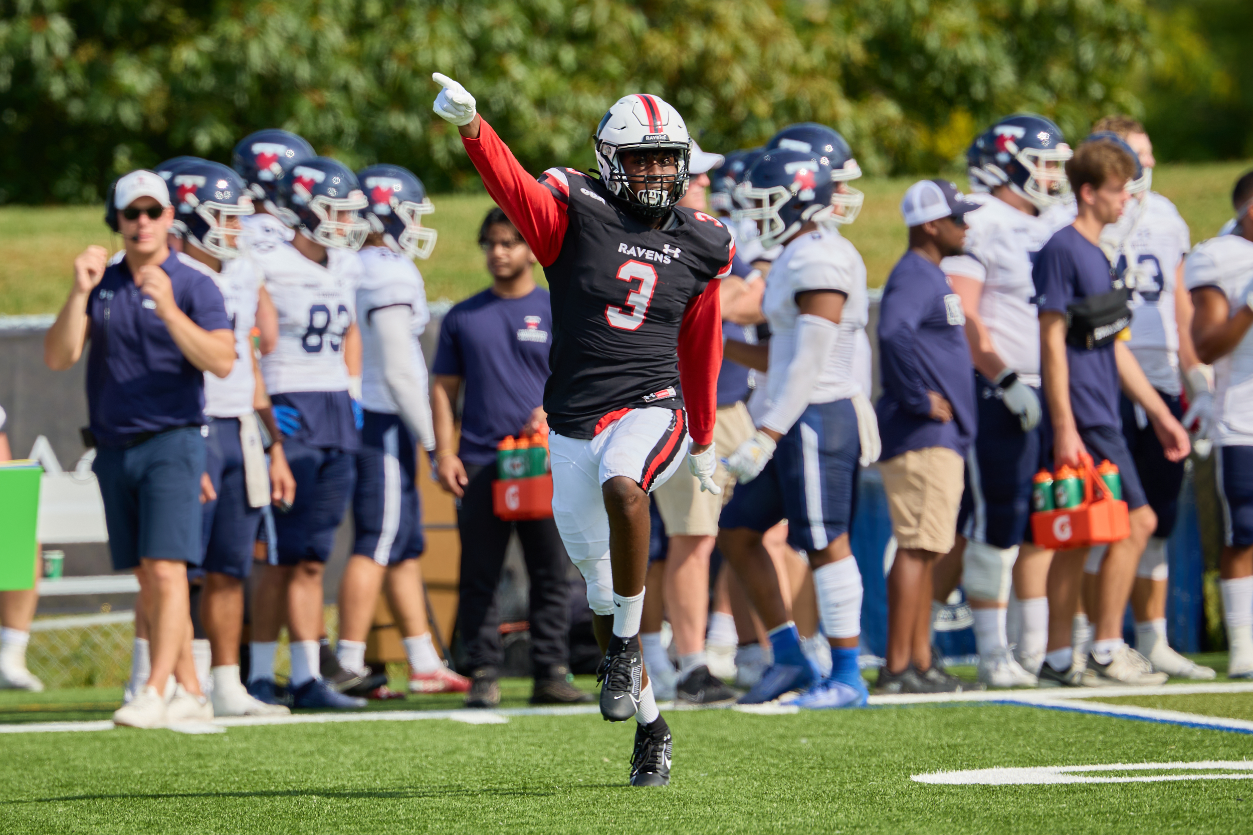 Member of Men's Football team running accross the field with hand pointed to the end zone.