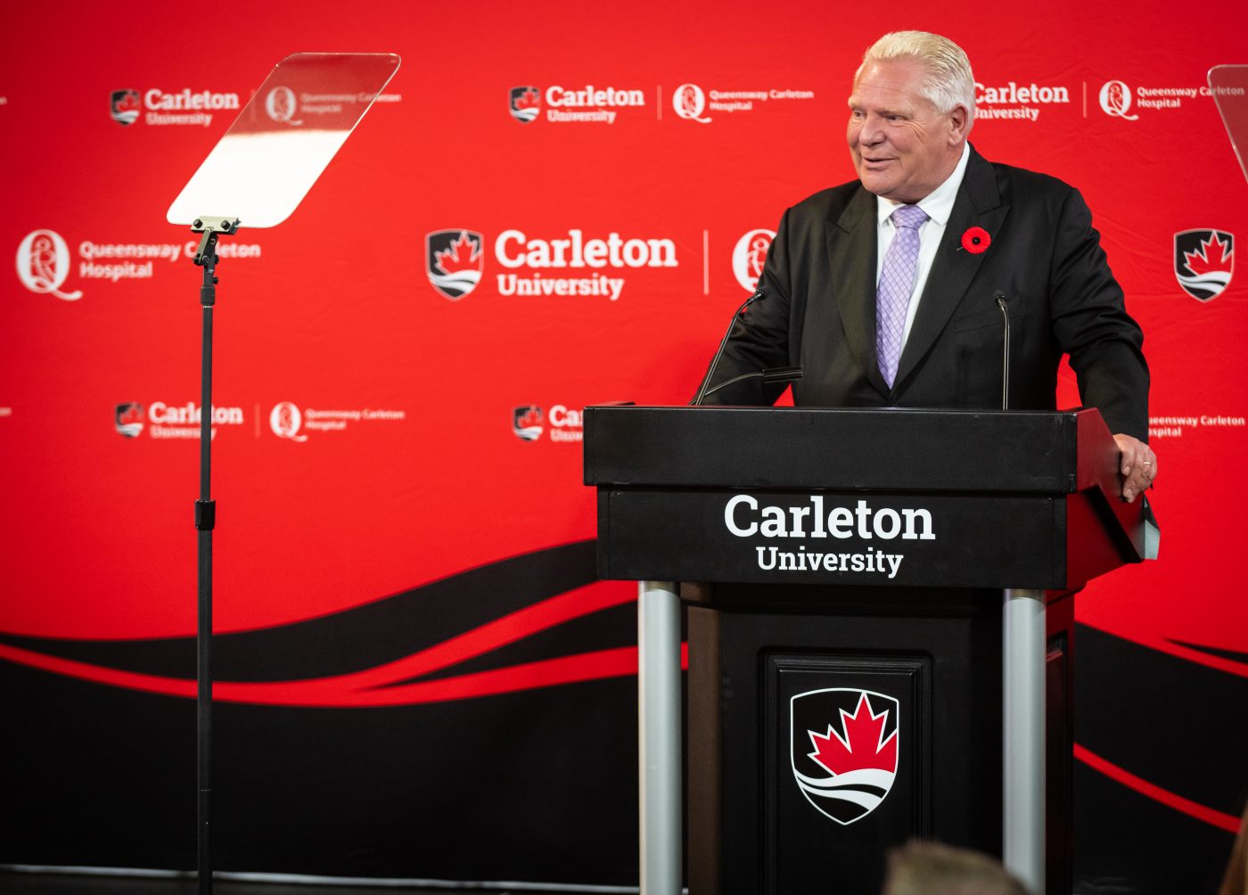 Premier Doug Ford standing at a podium in front of a red backdrop