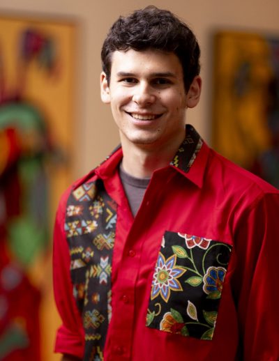 A man in a red shirt with black hair smiles at the camera