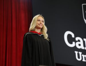 A blonde woman stands on the Convocation stages and smiles at the crowd
