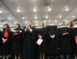 A row of Carleton graduates in black gownsstand and clap for their classmates at Carleton's Convocation