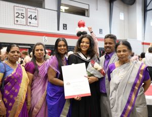 A Carleton graduate in a black gown poses with her family and smiles