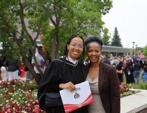 A Carleton graduate holds her degree and smiles while posing with a family member