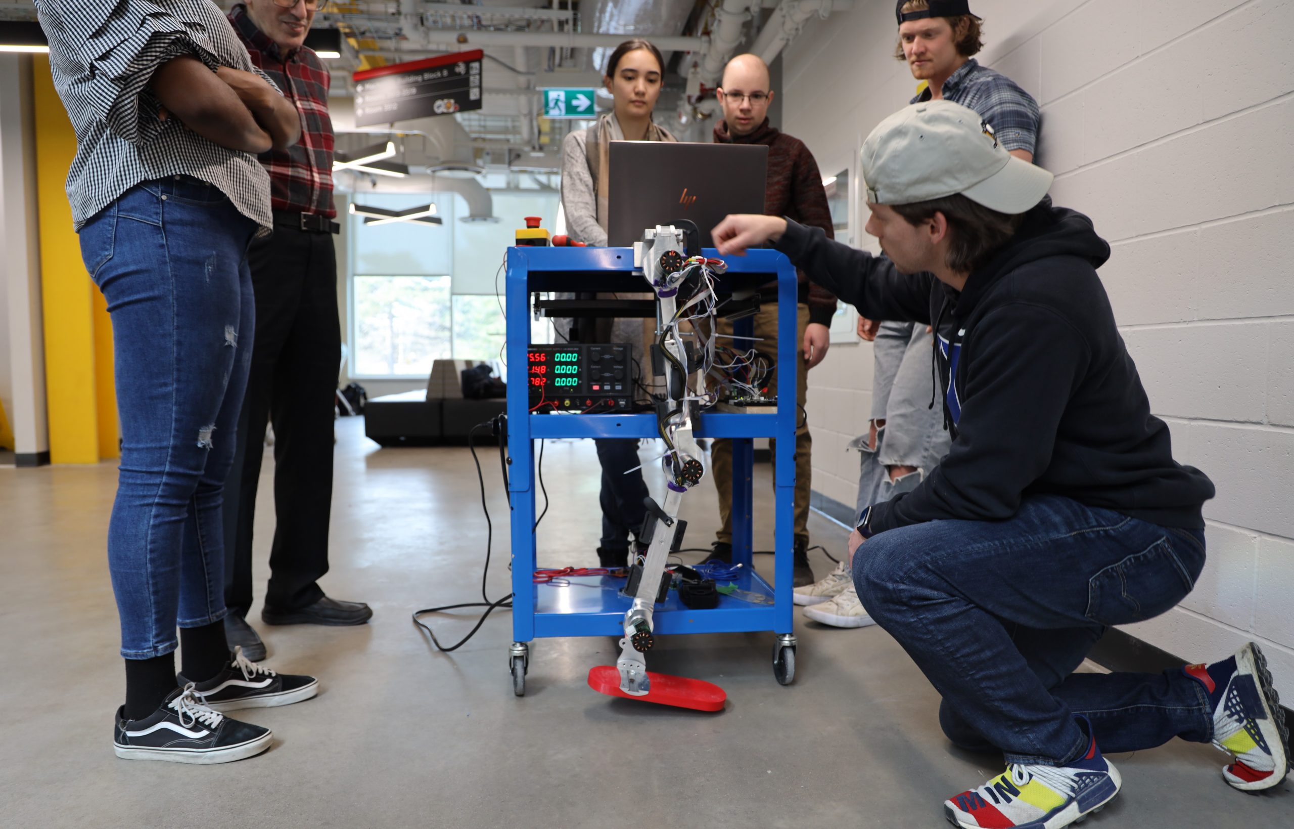 A group of people surround a robot leg they are looking at