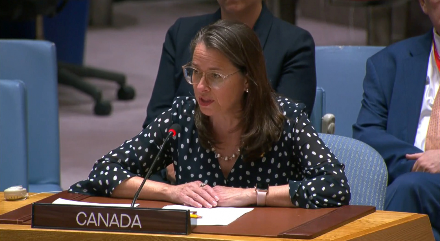 woman sitting at a desk in a chamber providing speech at the microphone