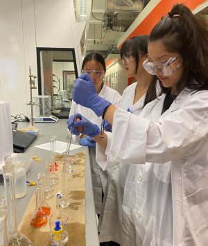 Three young women in lab coats exploring iron concentration workshop in Carleton’s chemistry superlab.