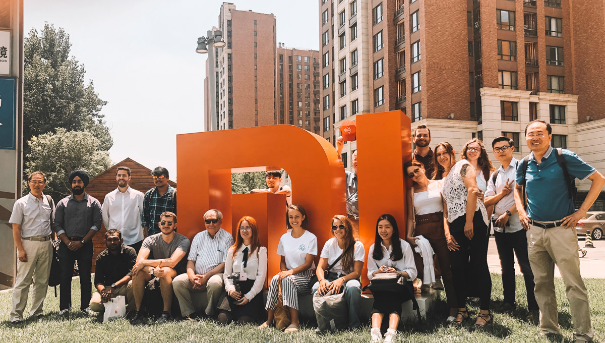 The Carleton delegation gathers around a large, three dimensional version of the Xiaomi logo in an outdoor setting.