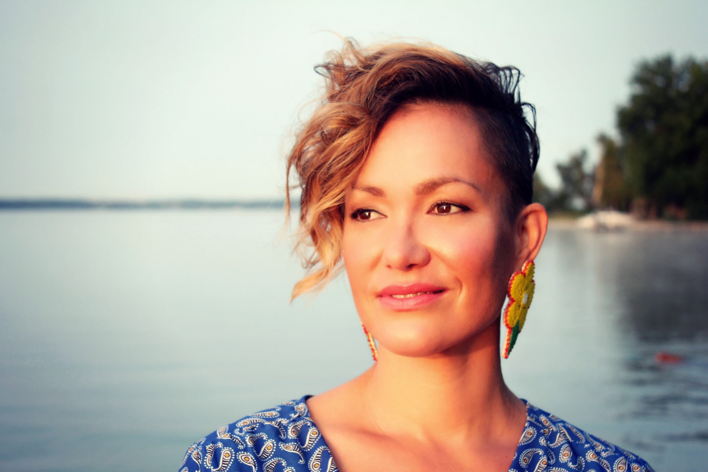 A woman with short brown hair stands in front of a lake