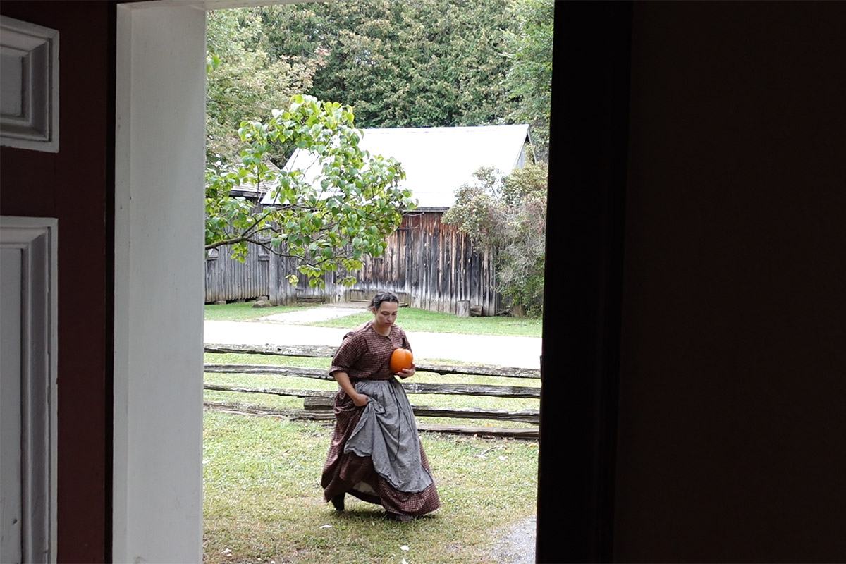 In a display of Canadian culinary history, a woman wearing old-fashioned clothing walks while holding a pumpkin.