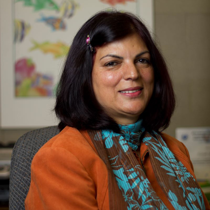 A woman with dark hair and an orange sweater smiles for the camera.