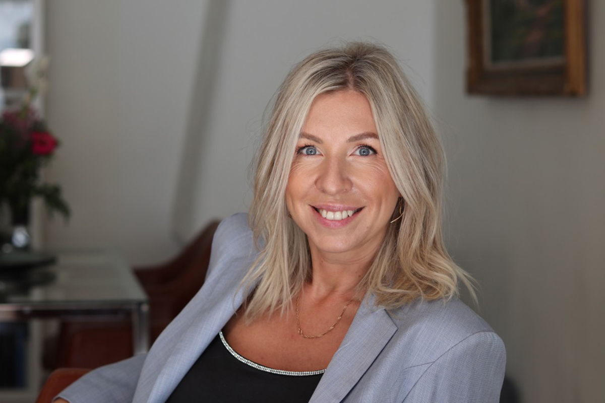 A professional headshot of a woman with a grey suit and black shirt.