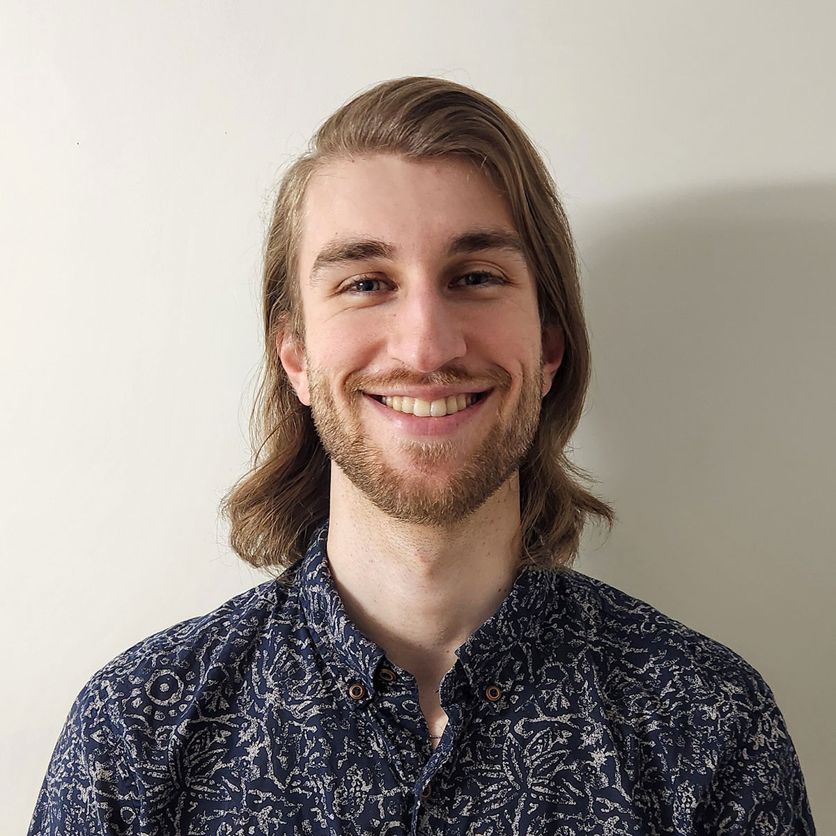 A headshot of a young man with long blonde hair and a blue button up shirt.