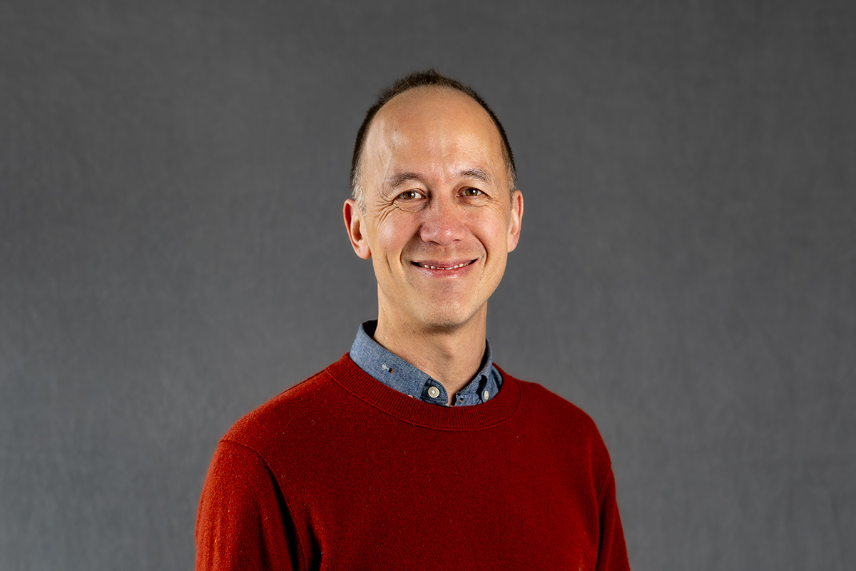 A professional headshot of a man with a red sweater.