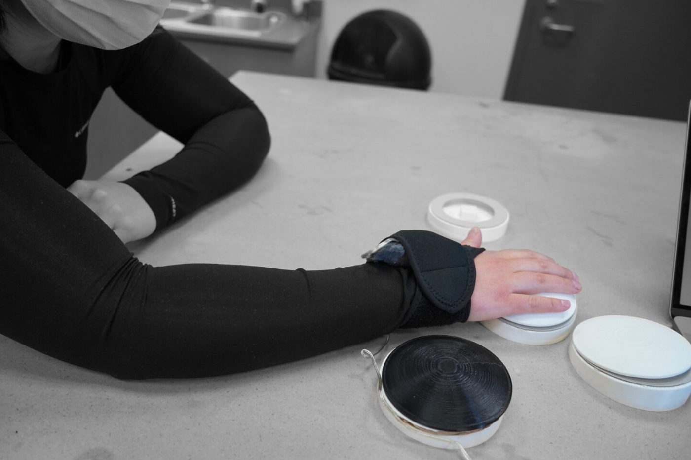 A hand with a black hand wrap is rested on a white circular device
