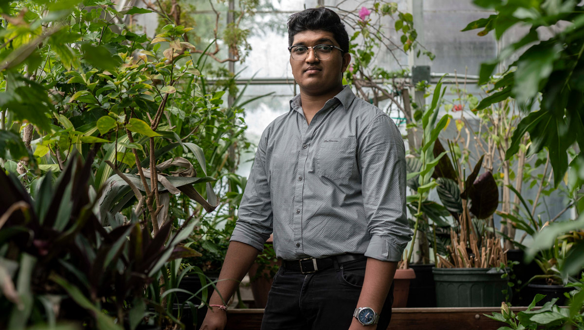 Bhavya Mohan poses in a greenhouse surrounded by plants.