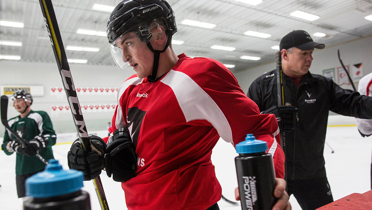 A photo of a male Carleton Ravens hockey player reaching for a water bottle on the bench.
