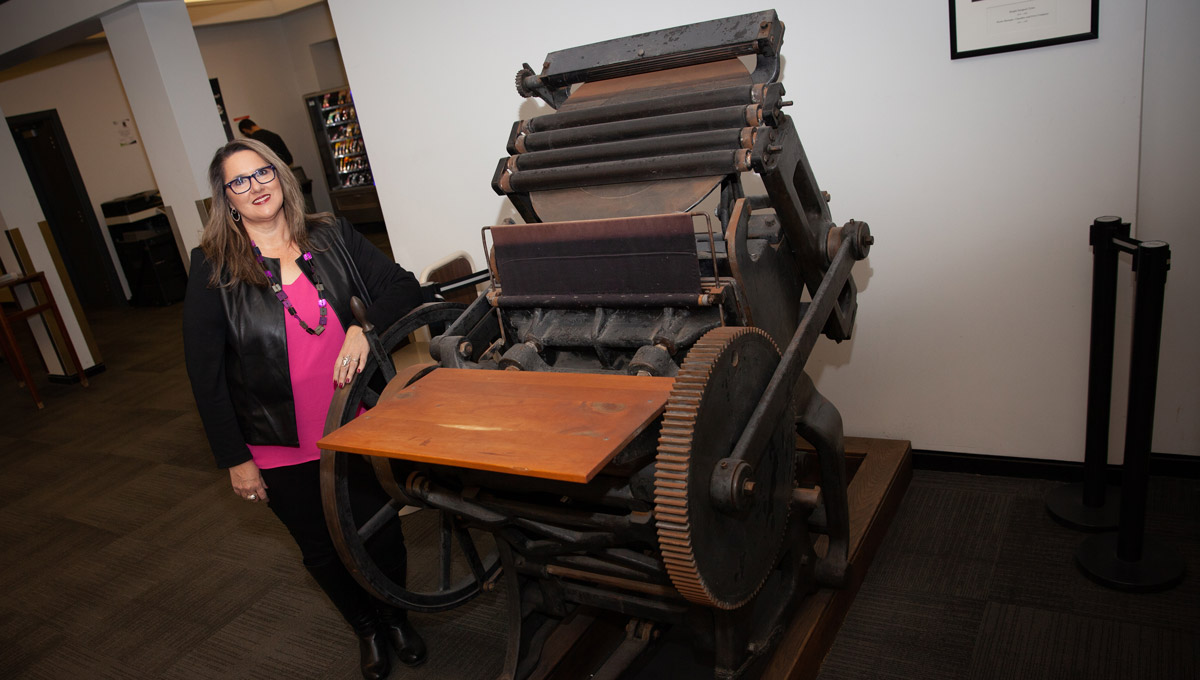 Patti Harper stands next to an antique printing press.