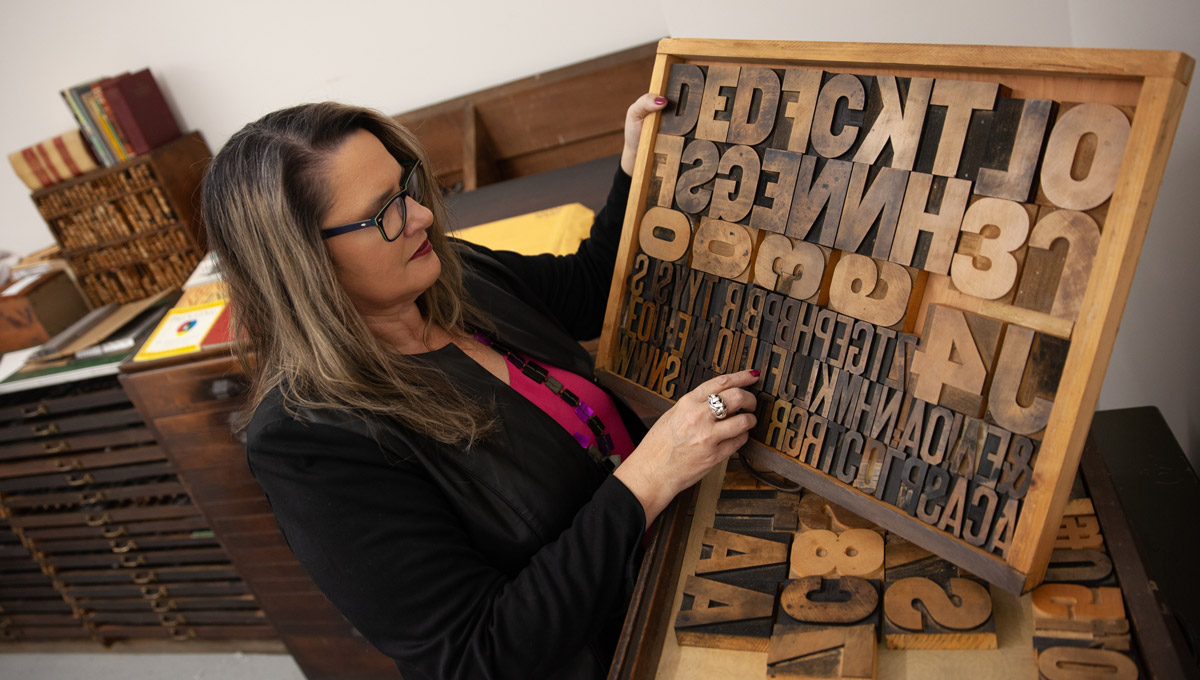 Patti Harper holds a box full of typeset letters in various fonts and sizes.