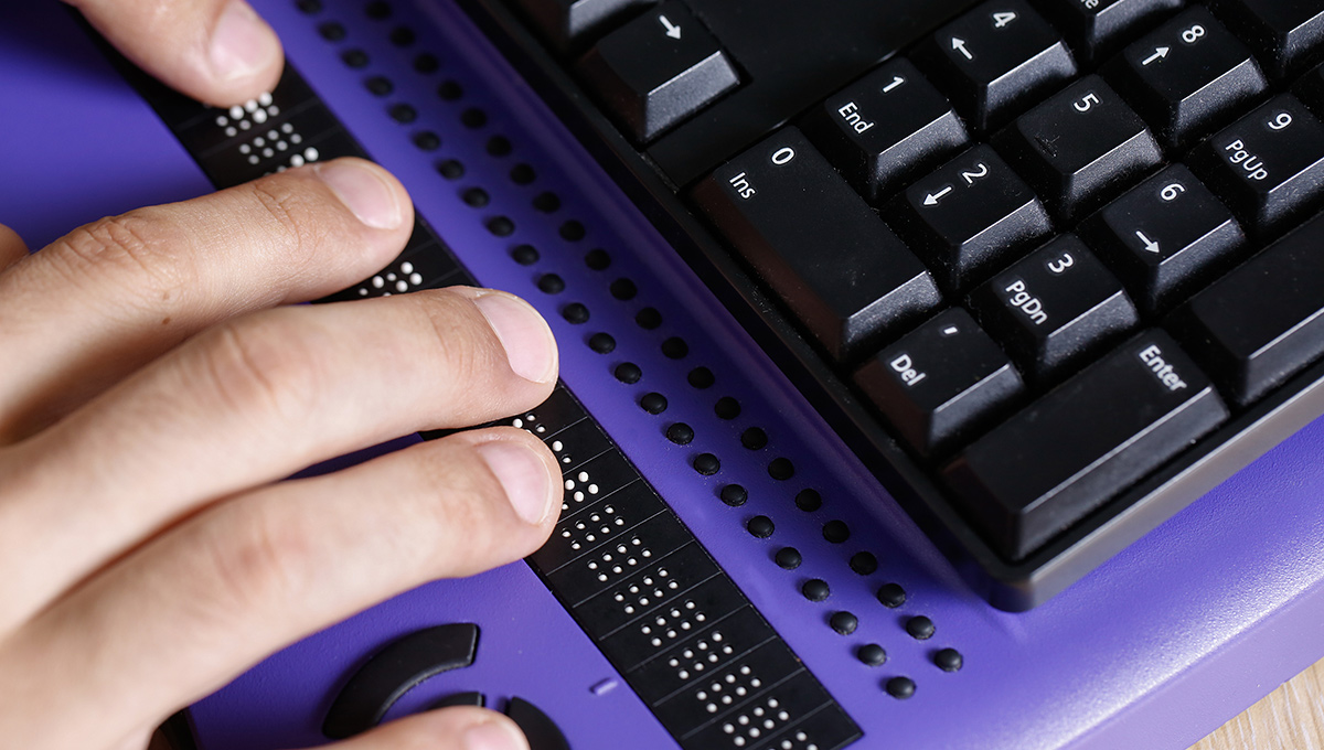 A hand is seen touching a braille computer keyboard