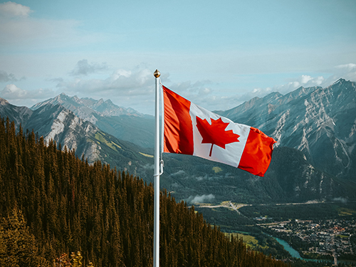 Canadian flag with mountains and trees in the background.