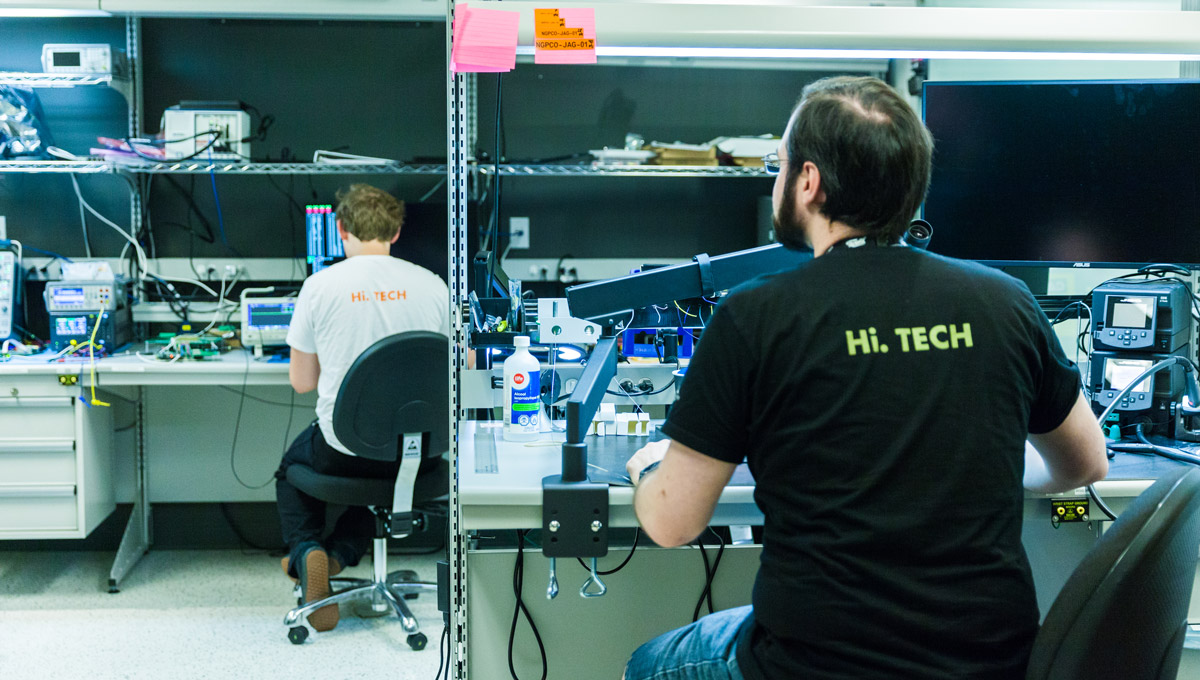 Carleton interns work at desks wearing t-shirts with the term "Hi. Tech" on them, surrounded by lab equipment.