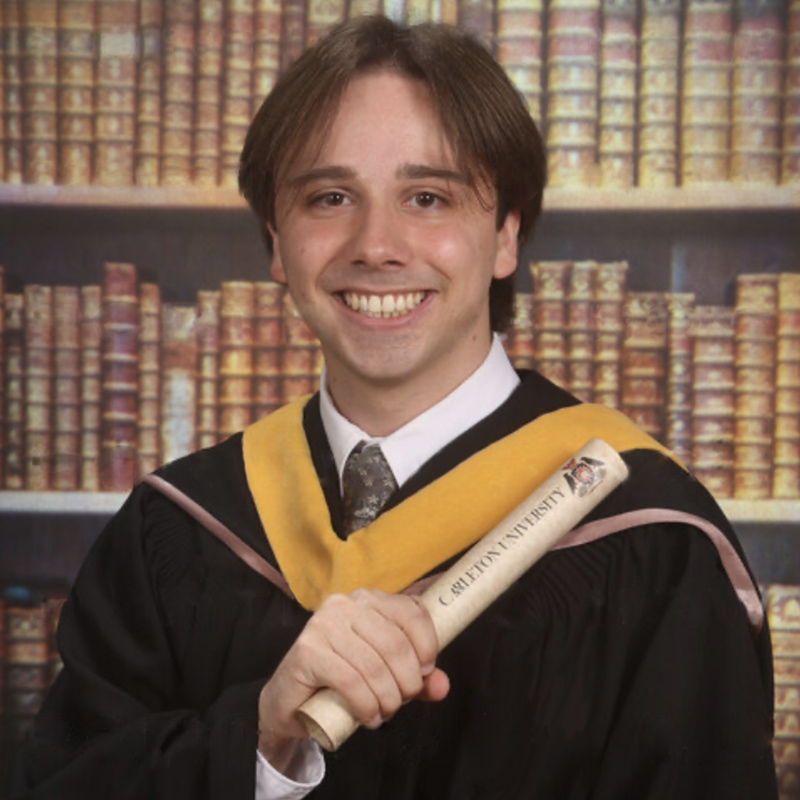 A young man dressed in academic regalia poses for the camera while holding a degree