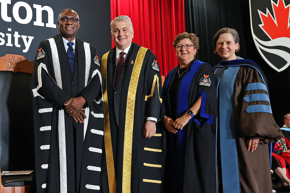 Four people wearing academic regalia posing for a group photo.