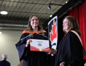 A graduate receives a degree on stage as Carleton Celebrates Fall Graduates