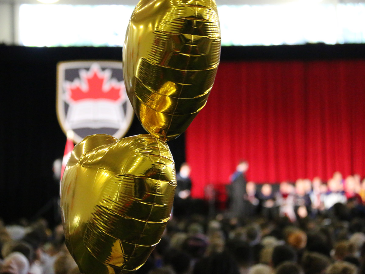 Balloons float in the Fieldhouse as a crowd watches graduates receive their degrees on stage.