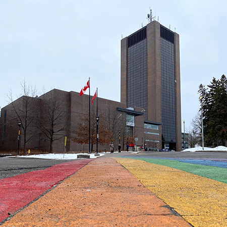 A ground level view of a rainbow road with a tall building, Dunton Tower, visible in the background