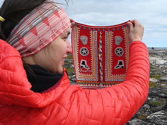 A woman holds up a sample of Inuit sewing and beading technologies.