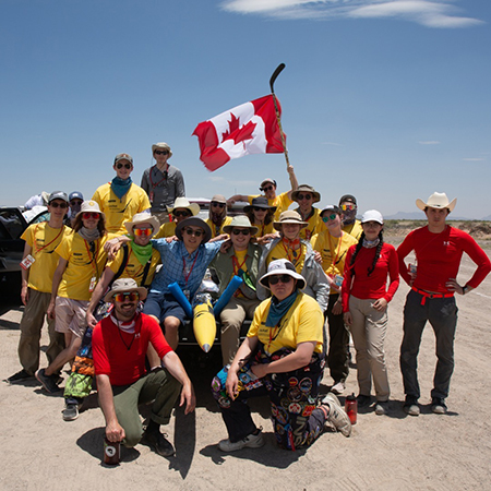 A large group of people wearing yellow shirts pose for a group shot with the Canadian flag visible behind them.